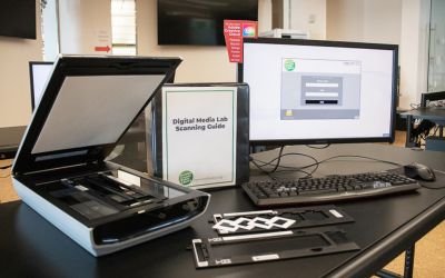 Flatbed scanner with the lid open. Scanner guide, optional scanner parts and computer are next to the scanner.