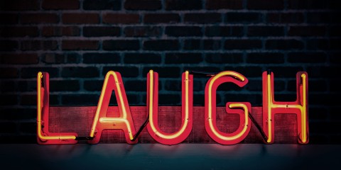 Photograph of neon lettering spelling out the word "laugh" in orange in front of a dark brick background