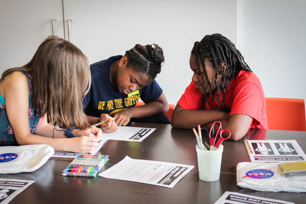 three teens sitting at a table working together to design their spacesuit