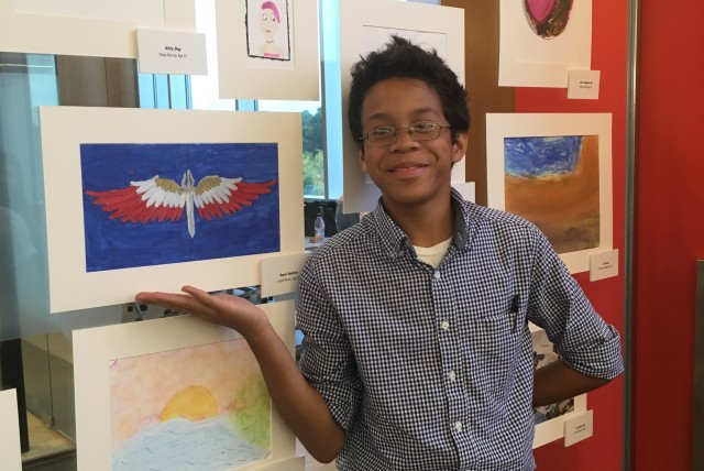 Artist standing next to their work, an image of a winged sword with blue background.