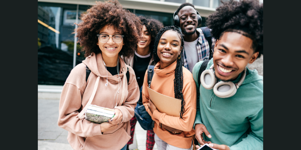 Five teen students stand in a group and smile toward the camera. They carry notebooks, backpacks, and some wear headphones. 