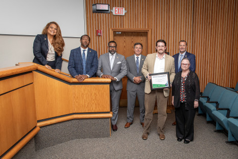 Seven individuals stand at the front of a boardroom and pose with an award.