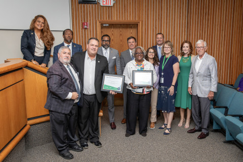 Twelve individuals stand at the front of a boardroom and pose with an award.