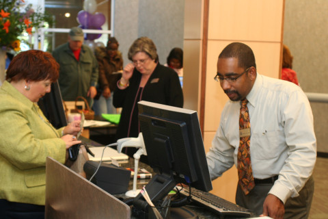 Two staff assist a group of patrons at a library circulation desk. 