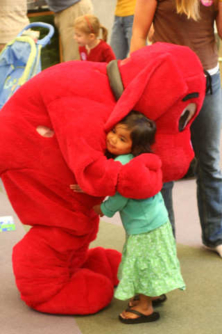 A Clifford the Big Red Dog mascot hugs a young child.