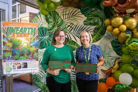 Two staff stand side-by-side holding signs. The sign on the left reads, 