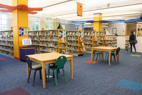 A wide shot features several book shelves and children's tables and chairs. 