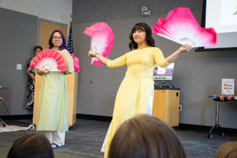 Two young women perform a traditional Vietnamese dance with bright pink and white folding fans. 