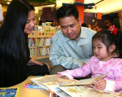 Two parents and their young child read picture books together in the children's area.