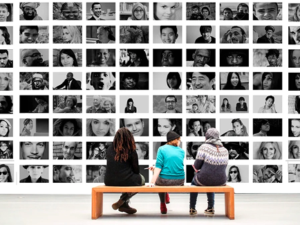 Three people sitting on a bench looking at photos on a wall.
