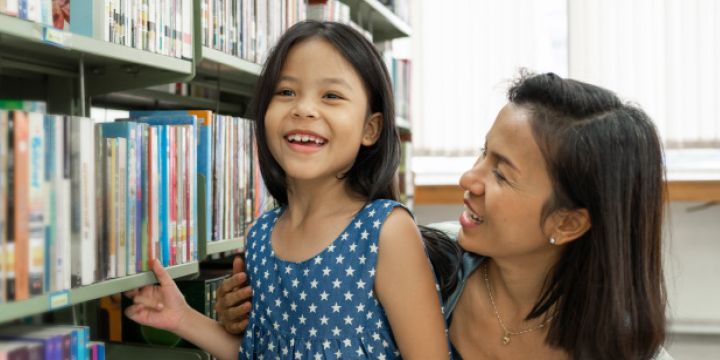 Mom smiling at daughter in front of library bookshelf